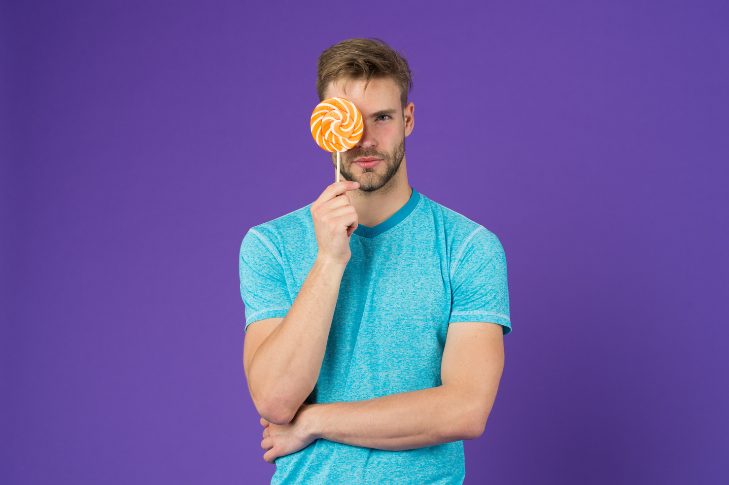Man with bristle likes lollipop. Cheat meal concept. Sugar harmful for health. Guy hold lollipop candy violet background. Taste of childhood. Lollipop fun. Man eat big colorful sweet lollipop