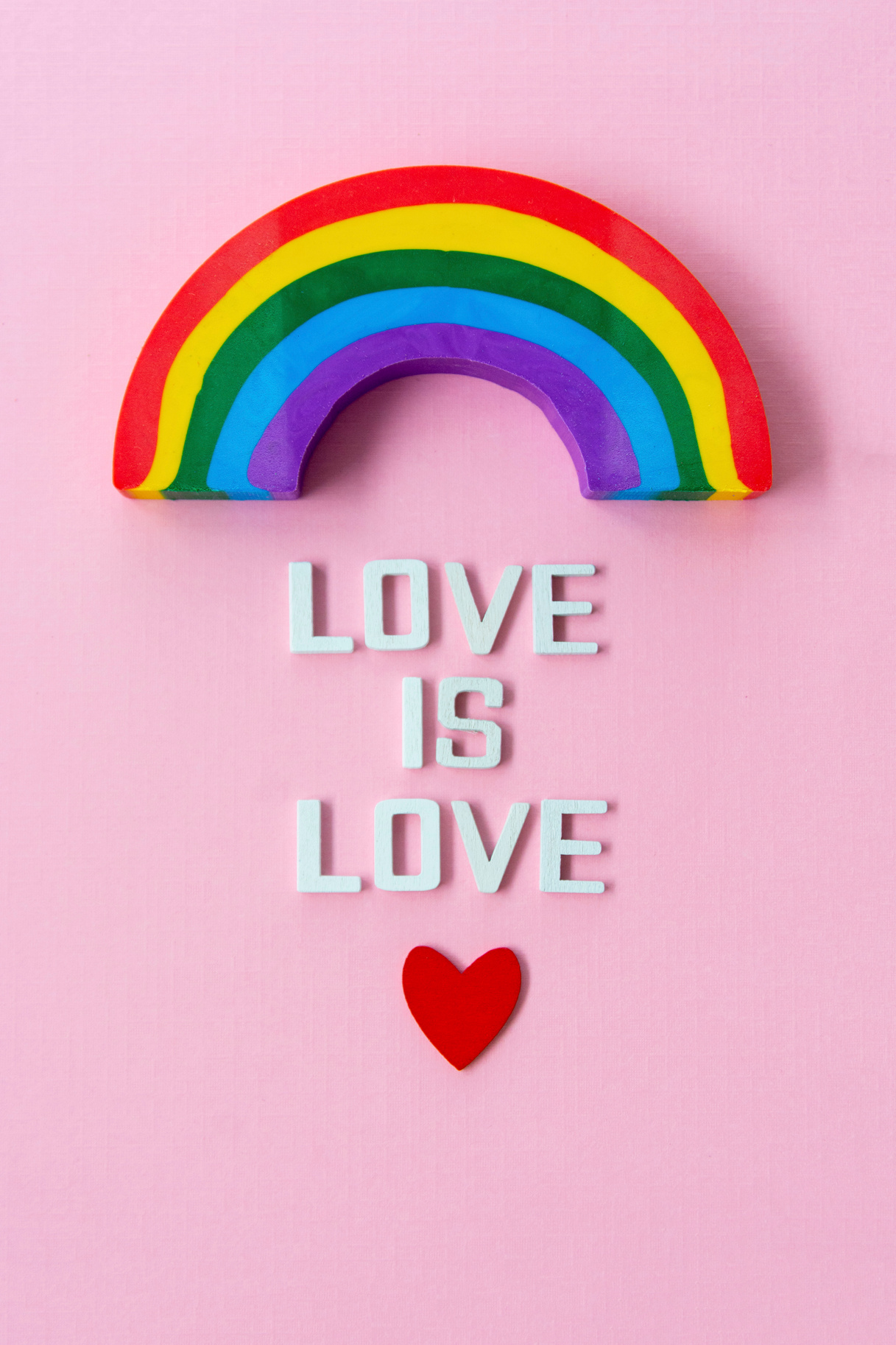 LGBT pride concept. Text LOVE IS LOVE with rainbow over pink background, top view.